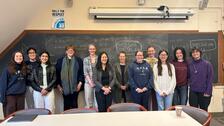 group of people standing in a line in front of a blackboard smiling.